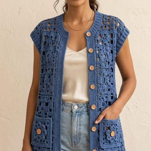 May include: A blue sleeveless crochet cardigan featuring a square floral motif pattern, a scalloped hem, and a front button closure with light brown wooden buttons. The garment includes two front patch pockets, each adorned with a matching floral square.