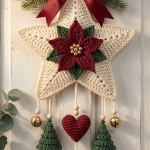 May include: A cream-coloured crocheted star wall hanging featuring a dark red poinsettia, a central red crocheted heart, two green crocheted trees, and gold jingle bells. The star is adorned with a dark red satin bow and red berry sprigs.