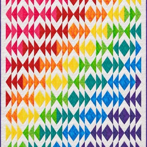 May include: A rectangular quilt featuring a vibrant rainbow gradient of geometric diamond and triangle shapes. The pattern transitions from pink and red on the left to orange, yellow, green, blue, and purple on the right, all set against a white background with a thin purple border.