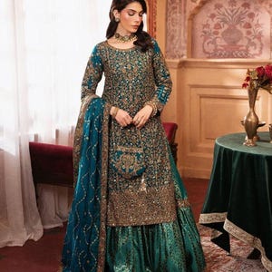 May include: A teal long-sleeved tunic and matching flared skirt set featuring intricate gold embroidery, sequins, and beadwork. The ensemble includes a coordinating teal dupatta with gold trim and a small matching embroidered handbag.