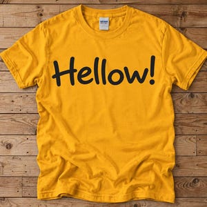 May include: A mustard yellow short-sleeved crew neck t-shirt featuring the word Hellow! printed in a bold black sans-serif font across the chest. The garment includes a white Gildan brand label at the inner neckline and has a standard fit.