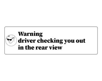 May include: A rectangular white sticker featuring black text that reads Warning driver checking you out in the rear view. To the left of the text is a circular black and white line drawing of a person wearing sunglasses and a baseball cap.