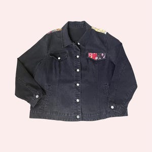 Peut inclure: Une veste en jean noire dotée d'un col classique, de manches longues avec poignets boutonnés et d'une fermeture à boutons sur le devant. Le vêtement comprend deux poches poitrine à rabat, dont l'une est ornée d'un tissu à motifs multicolores.