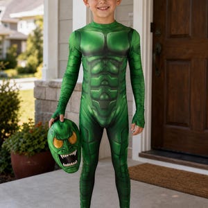 May include: A green full-body jumpsuit featuring a printed muscular armour design with long sleeves and integrated foot coverings. The garment is paired with a matching green mask that displays sharp white teeth and large yellow eyes.