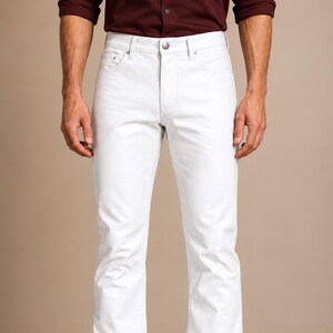 May include: A pair of solid white denim jeans featuring a classic five-pocket design, a metal button closure at the waist, and a straight-leg cut. The jeans are styled with a dark maroon long-sleeve shirt tucked in and black leather dress shoes.
