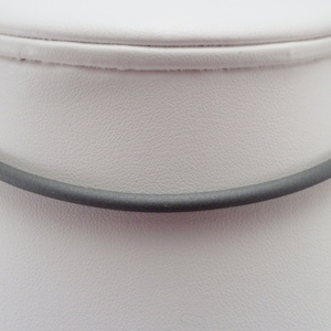 May include: A simple, dark gray choker necklace made of a smooth, flexible material. The necklace is shown on a white mannequin.