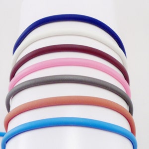 May include: A set of seven colorful silicone wristbands in blue, orange, gray, pink, maroon, white, and navy blue.