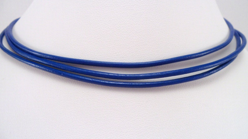 May include: A triple-strand blue leather cord necklace. The cord is smooth and has a slight sheen.