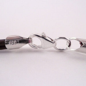 May include: Close-up of a brown leather cord necklace with a silver clasp. The clasp is marked with "925."