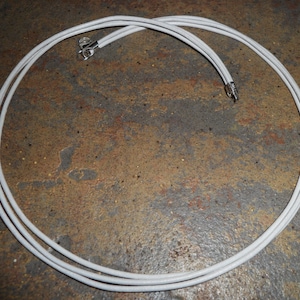 May include: A white cord with two metal ends, coiled into a circle.