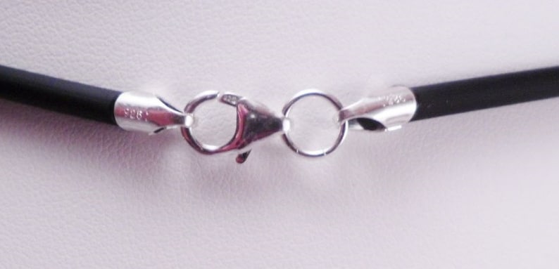 May include: Close-up of a silver clasp on a black cord necklace.