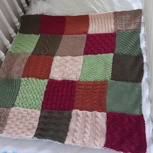 May include: A knitted baby blanket with a patchwork design in shades of green, brown, red, and cream. The blanket is made up of squares with different knit patterns.