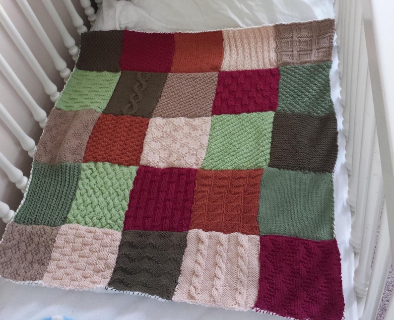 May include: A knitted baby blanket with a patchwork design in shades of green, brown, red, and cream. The blanket is made up of squares with different knit patterns.