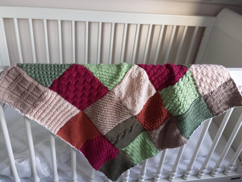 May include: A multi-coloured knitted baby blanket with a patchwork design. The blanket is made of different shades of green, red, brown, and pink.