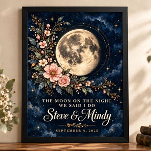 May include: A framed rectangular print featuring a large full moon against a dark blue starry night sky. A floral arrangement of pink flowers and green leaves curves around the moon. Text reads: THE MOON ON THE NIGHT WE SAID I DO, Steve & Mindy, SEPTEMBER 9, 2025.