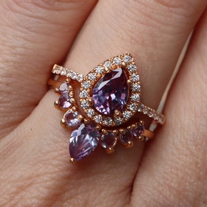 May include: A rose gold ring set with a large pear-shaped amethyst surrounded by smaller diamonds. The ring is accented with smaller amethyst stones in a delicate floral design.