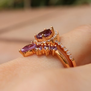 May include: A gold ring with a cluster of purple gemstones and a band of smaller white gemstones.