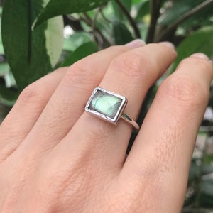 May include: A silver ring with a rectangular green labradorite gemstone.