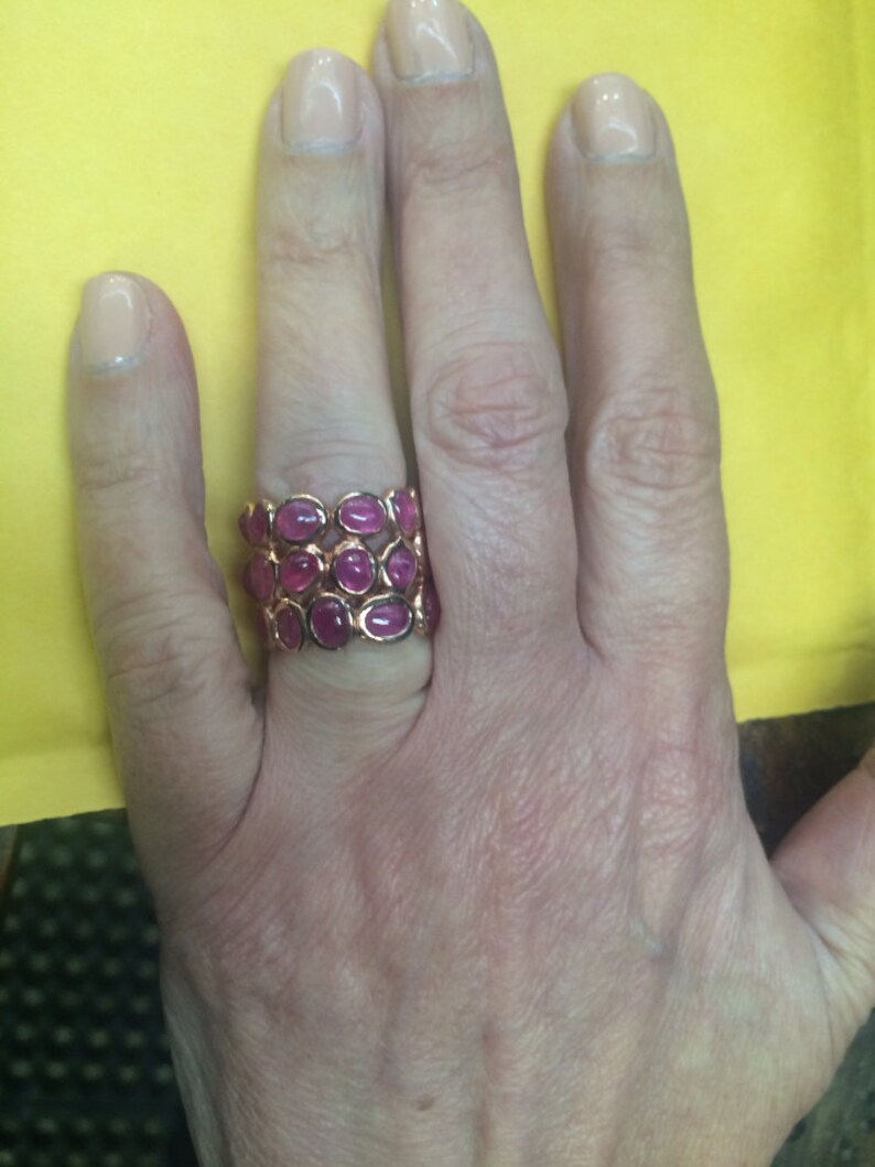 May include: A gold ring with multiple rows of oval-shaped pink gemstones. The ring is worn on a person's finger.