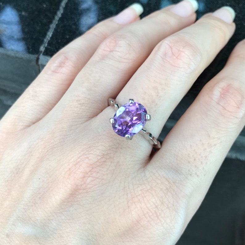 May include: A silver ring with a large oval amethyst gemstone. The ring has a twisted band.