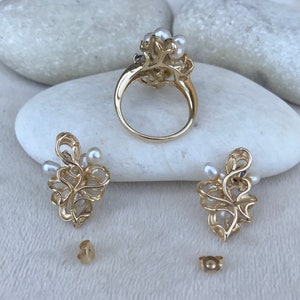 May include: A gold ring and earrings set with a delicate floral design and white pearls. The ring has a wide band and the earrings are drop style.