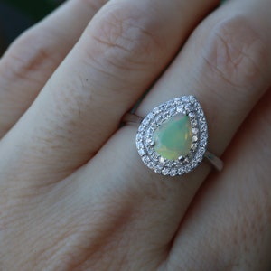 May include: A pear-shaped opal ring with a double halo of clear cubic zirconia stones set in sterling silver.
