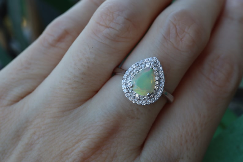 May include: A pear-shaped opal ring with a double halo of clear cubic zirconia stones set in sterling silver.