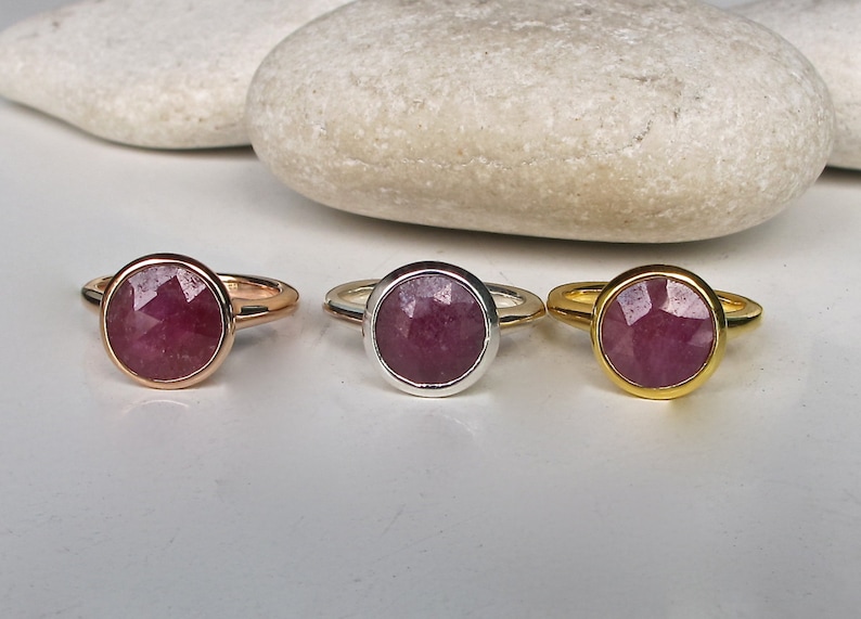 Pu&ograve; includere: Tre anelli con una pietra preziosa rotonda e sfaccettata di colore rosa incastonata in una montatura a castone. Gli anelli sono mostrati su uno sfondo bianco. Gli anelli sono disponibili in oro, argento e oro rosa.