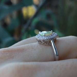 May include: A silver ring with a pear-shaped green opal gemstone surrounded by a halo of smaller clear gemstones.