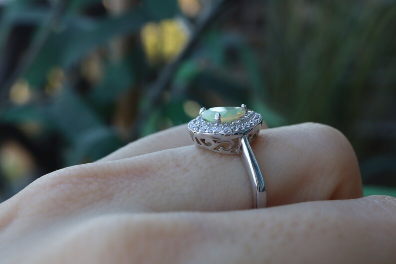 May include: A silver ring with a pear-shaped green opal gemstone surrounded by a halo of smaller clear gemstones.