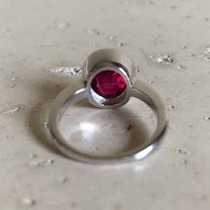 May include: A silver ring with a round, bright red gemstone set in a bezel setting.