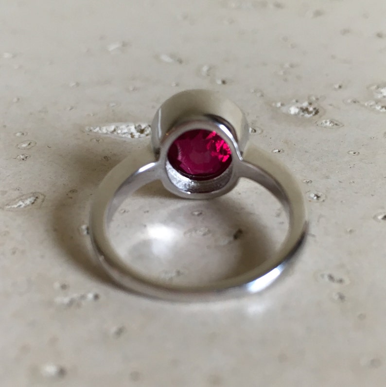 May include: A silver ring with a round, bright red gemstone set in a bezel setting.