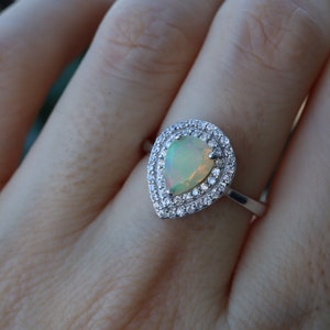May include: A pear-shaped opal ring with a double halo of clear cubic zirconia stones set in sterling silver.