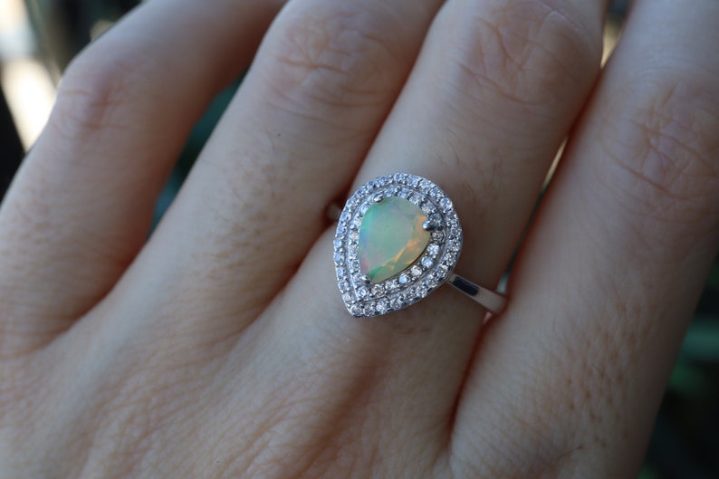 May include: A pear-shaped opal ring with a double halo of clear cubic zirconia stones set in sterling silver.