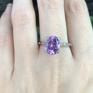 May include: A silver ring with a large oval amethyst gemstone. The ring has a twisted band.