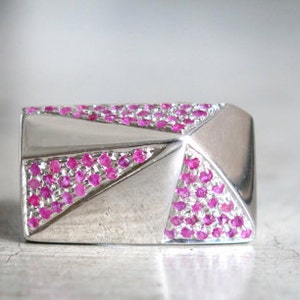 Pode incluir: Um anel de prata com um design geométrico e pedras preciosas cor-de-rosa.