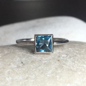 May include: A silver ring with a square-shaped blue topaz gemstone.