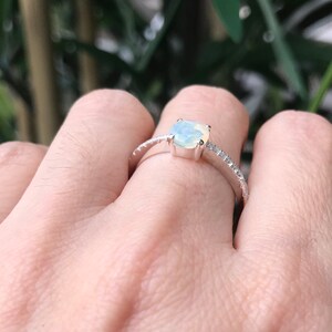 Pode incluir: Um anel de prata com uma pedra de opala branca e uma banda de pequenos diamantes.