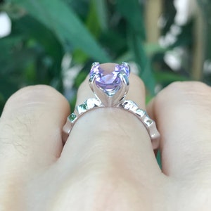 May include: A silver ring with a large, light purple gemstone set in a prong setting. The ring is on a finger.