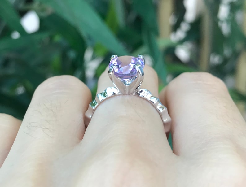 May include: A silver ring with a large, light purple gemstone set in a prong setting. The ring is on a finger.