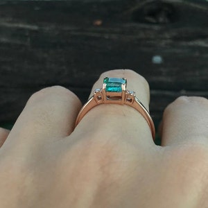 Op de afbeelding: Een ring van ros&eacute;goud met een groene smaragd en twee kleinere diamanten aan weerszijden.