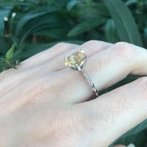 May include: A silver ring with a yellow gemstone set in a prong setting. The band is twisted and has a delicate design.