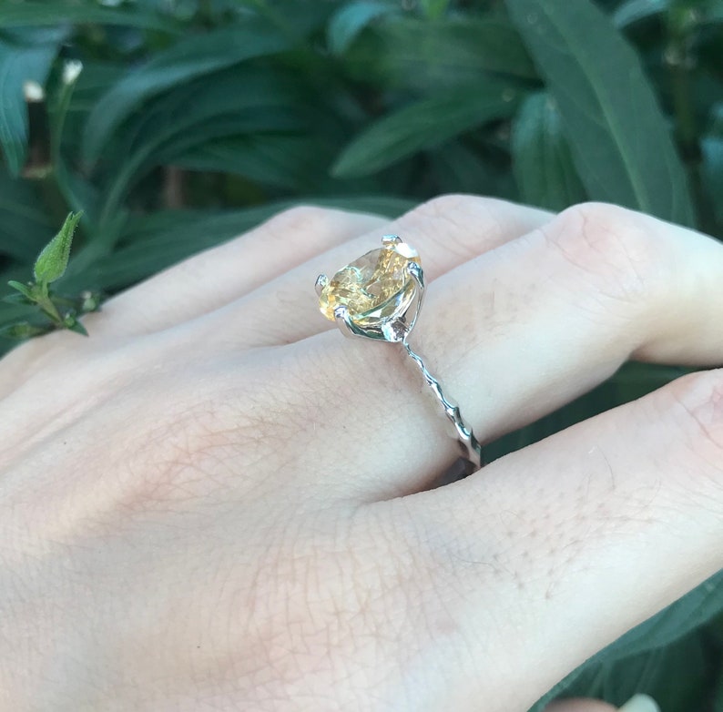May include: A silver ring with a yellow gemstone set in a prong setting. The band is twisted and has a delicate design.