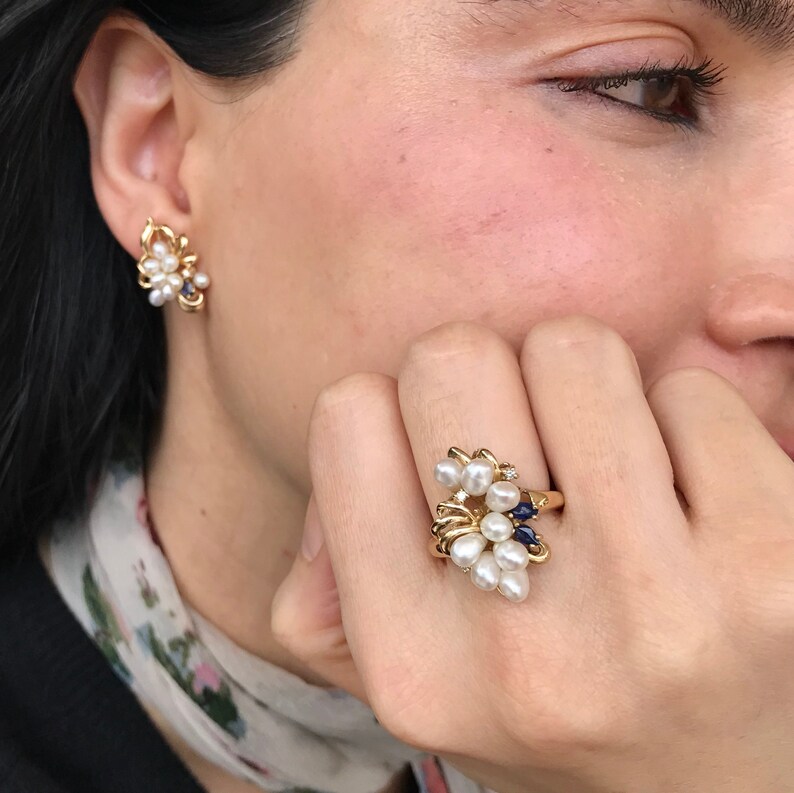 May include: A gold ring with a cluster of white pearls, blue sapphires, and a single diamond. The ring is set on a white background.