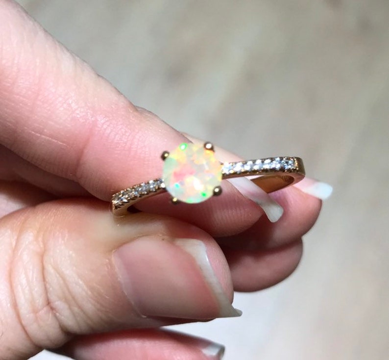Pode incluir: Um anel de ouro com uma pedra de opala branca e uma banda de pequenas pedras transparentes.