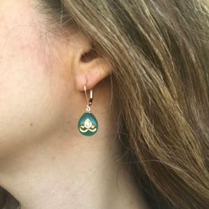 Op de afbeelding: Gouden oorhangers met een groene traanvormige steen en een gouden ontwerp in het midden.