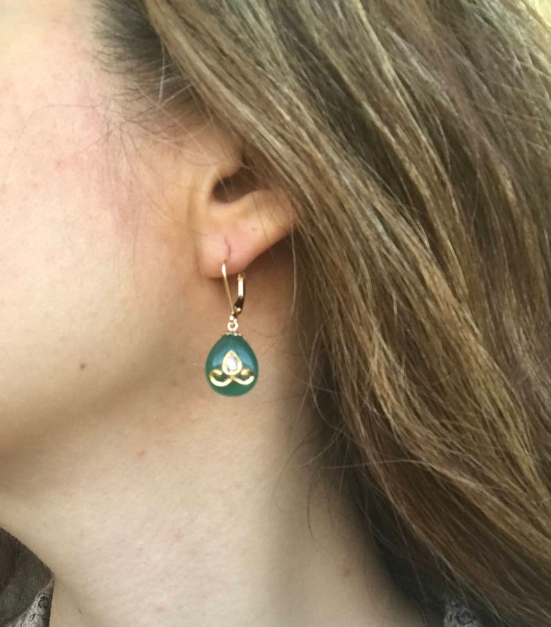 Op de afbeelding: Gouden oorhangers met een groene traanvormige steen en een gouden ontwerp in het midden.