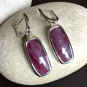 May include: A pair of silver dangle earrings with rectangular pink gemstones. The earrings have a simple, elegant design.