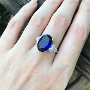 May include: A silver ring with a large oval-shaped blue sapphire gemstone surrounded by smaller white gemstones.