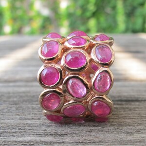 May include: A rose gold ring with multiple rows of pink oval-shaped gemstones.